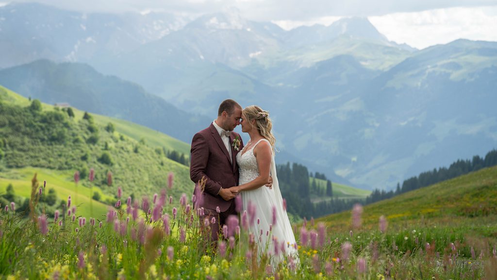 Bezaubernde Berghochzeit auf dem Hahnenmoos (Adelboden · Lenk) - Hochzeit von Laurence & Bryan 1 Braut und Bräutigam umarmen sich auf einer Blumenwiese auf dem Hahnenmoos bei Adelboden Lenk, umgeben von Berglandschaft im Berner Oberland - Berghochzeit wie im Bilderbuch