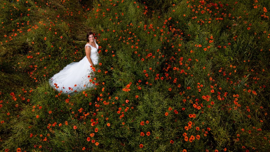 Braut geniesst den Moment beim After-Wedding-Shooting im Rapsfeld mit Mohnblumen aus der Luft in der Schweiz