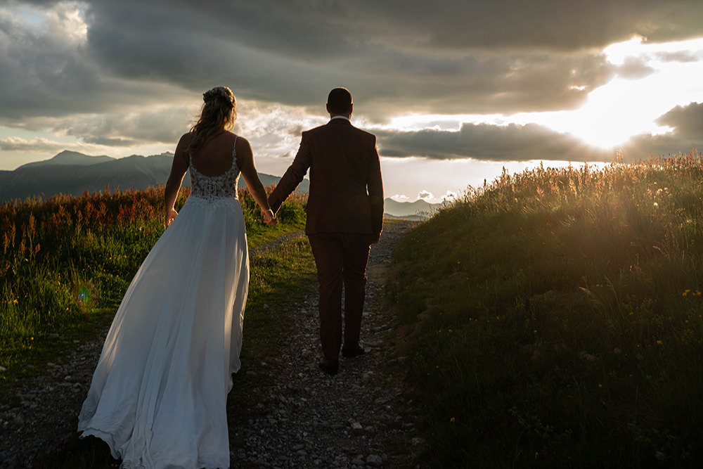 Braut und Bräutigam gehen Hand in Hand bei Sonnenuntergang auf dem Hahnenmoos in Adelboden Lenk durch die Berglandschaft.