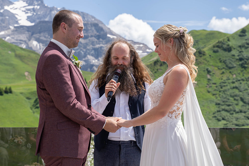 Bezaubernde Berghochzeit auf dem Hahnenmoos (Adelboden · Lenk) - Hochzeit von Laurence & Bryan 4 Freie Trauung auf dem Hahnenmoos bei Adelboden Lenk, Braut und Bräutigam halten sich an den Händen vor alpinem Bergpanorama.