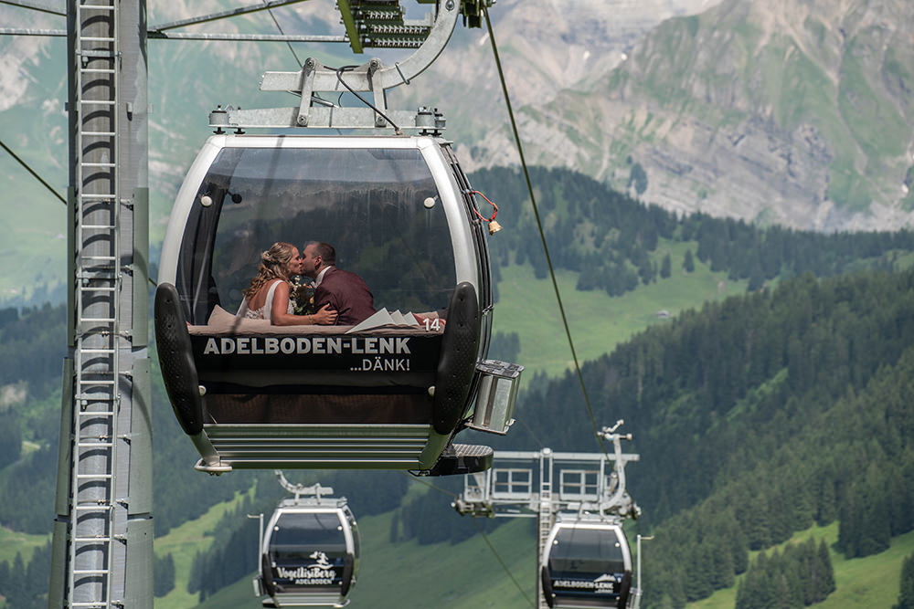Bezaubernde Berghochzeit auf dem Hahnenmoos (Adelboden · Lenk) - Hochzeit von Laurence & Bryan 5 Braut und Bräutigam küssen sich in einer Gondel über dem Hahnenmoos bei Adelboden Lenk, umgeben von Berglandschaft.